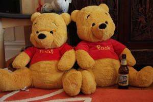 Two Pooh Bears sitting next to each other with a beer