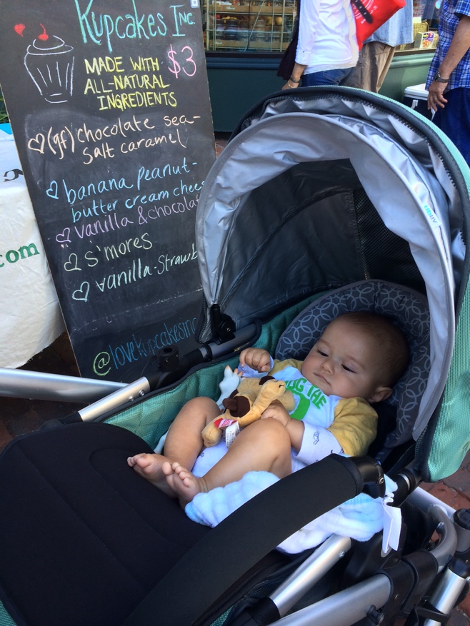 Baby in stroller in front of cupcake sign