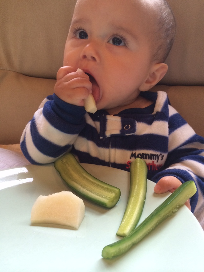 Baby with plate of food and pear in mouth