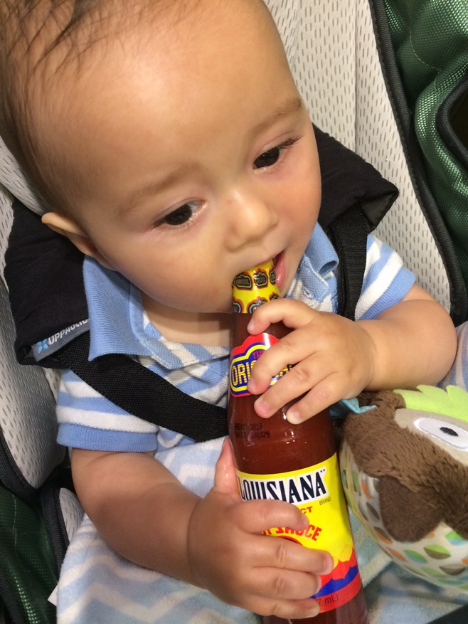 Baby biting on hot sauce bottle