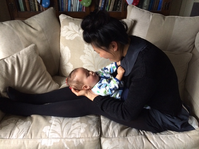 Baby lying on woman sitting on couch