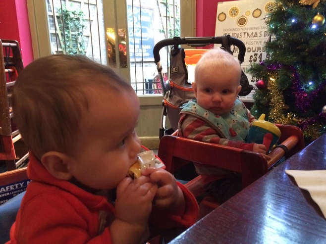 Two babies in high chairs with snacks