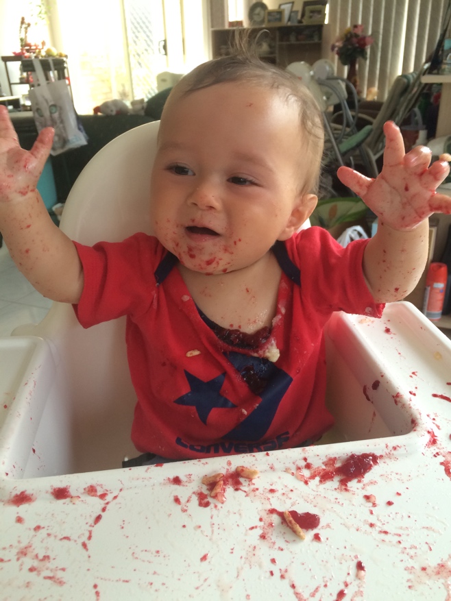 Baby with red plum mess all over his high chair