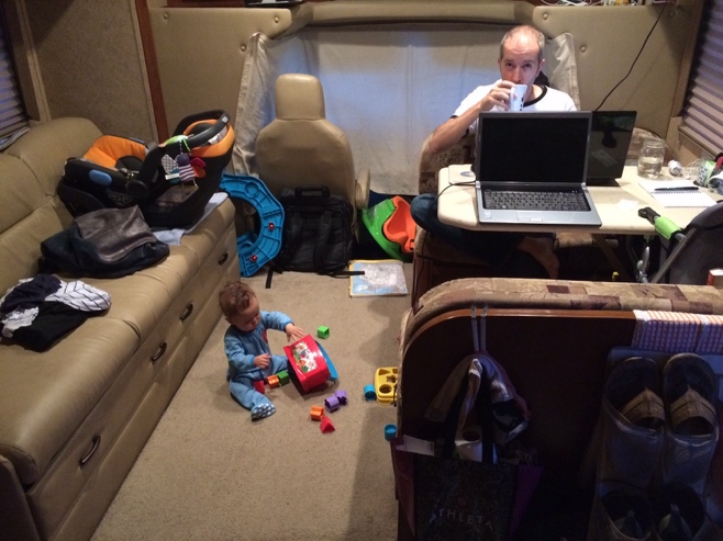 Baby playing on RV floor with dad at computer